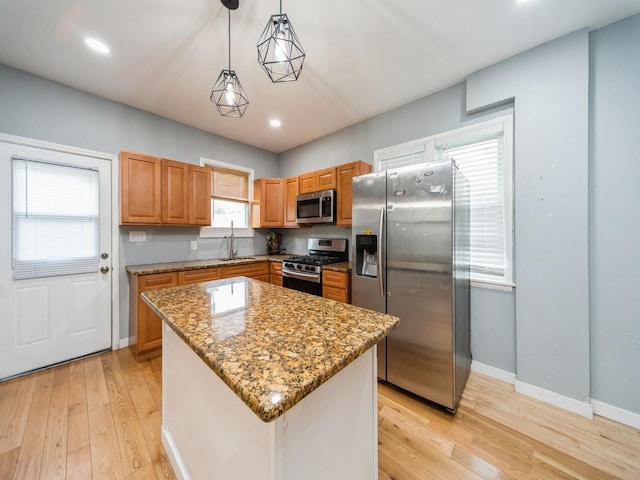 1534 9th St, Des Moines, IA 50314 - kitchen featuring stainless steel appliances, light wood-type flooring, light stone counters, a center island, and hanging light fixtures