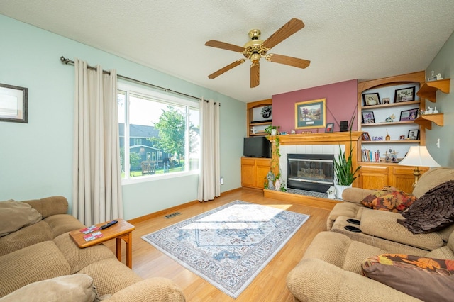 9102 NW Windsor Dr, Johnston, IA 50131 - living area featuring ceiling fan, a tile fireplace, light wood-style flooring, and a textured ceiling
