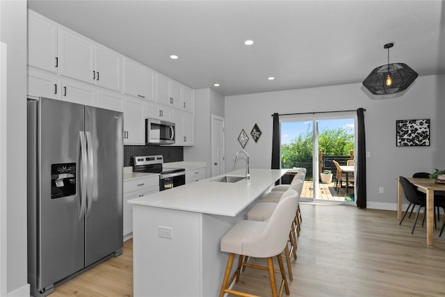 1375 SE Parkview Crossing Dr, Waukee, IA 50263 - kitchen with appliances with stainless steel finishes, white cabinetry, light wood finished floors, a center island with sink, and tasteful backsplash