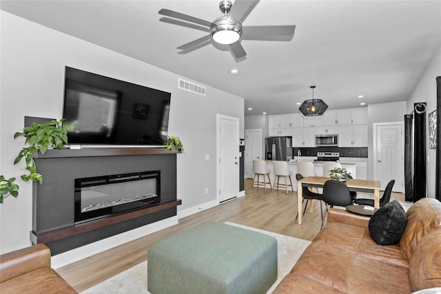 1375 SE Parkview Crossing Dr, Waukee, IA 50263 - living area featuring light wood-style flooring, a glass covered fireplace, a ceiling fan, and recessed lighting