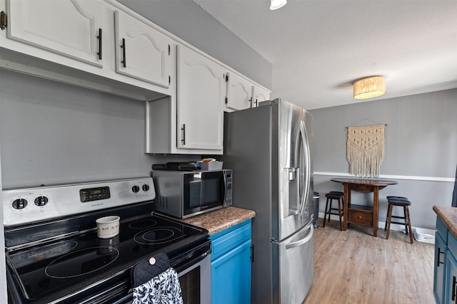 6675 NW 5th St, Des Moines, IA 50313 - kitchen featuring stainless steel appliances, white cabinetry, blue cabinetry, light wood-style flooring, and a textured ceiling