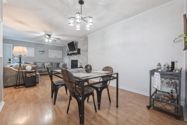 3504 56th St, Des Moines, IA 50310 - dining room featuring a fireplace, a ceiling fan, light wood-style flooring, crown molding, and a chandelier