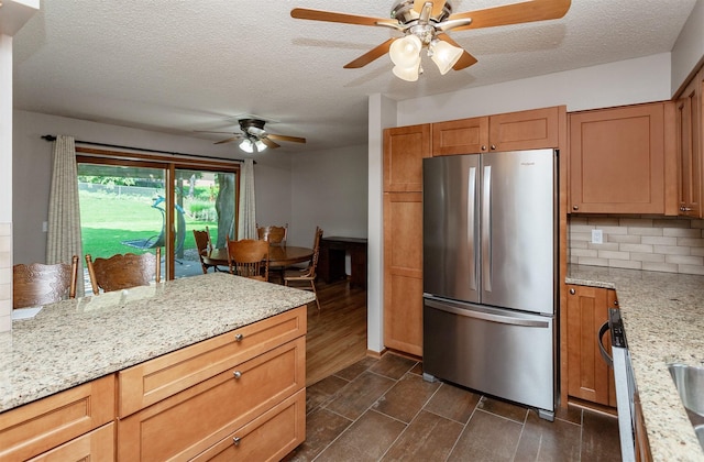 2726 Lakeland Dr, Urbandale, IA 50322 - kitchen with freestanding refrigerator, ceiling fan, a textured ceiling, decorative backsplash, and light stone counters