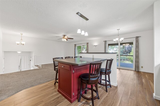 7005 Surrey Dr NE, Cedar Rapids, IA 52402 - kitchen with a chandelier, dark countertops, light wood finished floors, a breakfast bar area, and a textured ceiling