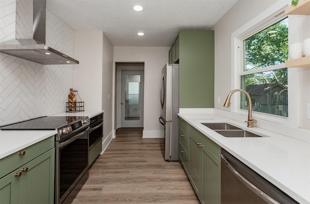 910 30th St, Des Moines, IA 50312 - kitchen featuring green cabinetry, wall chimney range hood, appliances with stainless steel finishes, backsplash, and light countertops
