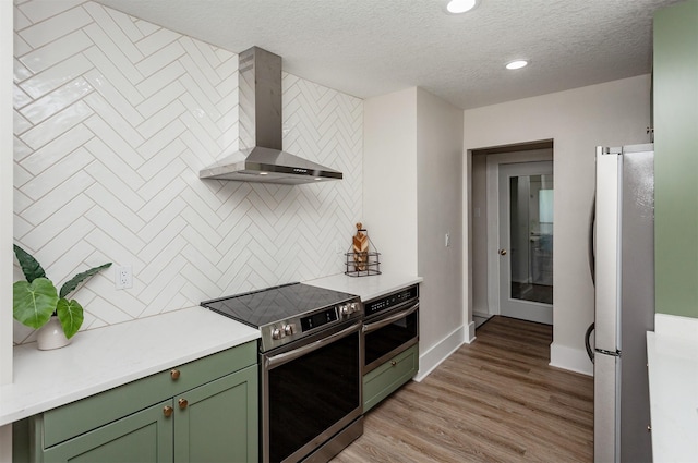910 30th St, Des Moines, IA 50312 - kitchen featuring green cabinets, stainless steel appliances, wall chimney range hood, decorative backsplash, and light countertops