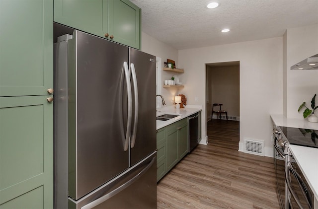 910 30th St, Des Moines, IA 50312 - kitchen with green cabinets, appliances with stainless steel finishes, light wood-type flooring, a textured ceiling, and light countertops