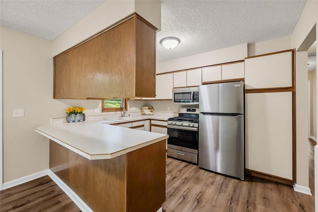 3312 Kinsey Ave, Des Moines, IA 50317 - kitchen with appliances with stainless steel finishes, a textured ceiling, a peninsula, light countertops, and wood finished floors