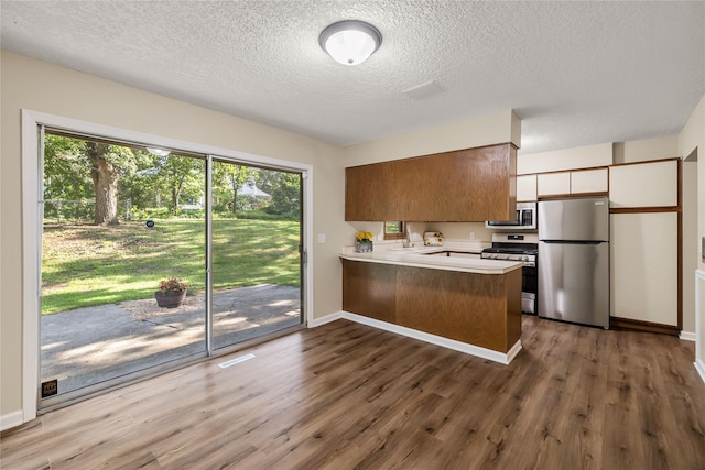 3312 Kinsey Ave, Des Moines, IA 50317 - kitchen featuring appliances with stainless steel finishes, a peninsula, wood finished floors, light countertops, and a textured ceiling