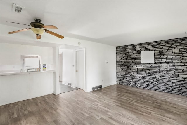1356 E 17th Ct, Des Moines, IA 50316 - unfurnished living room with ceiling fan, wood finished floors, and brick wall