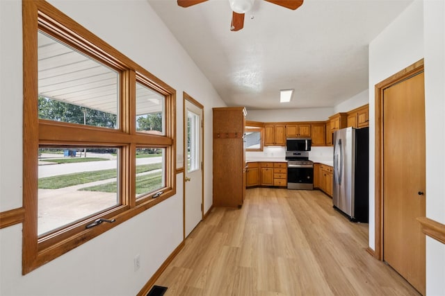 204 N Gaines St, Stuart, IA 50250 - kitchen with light wood finished floors, appliances with stainless steel finishes, light countertops, brown cabinetry, and ceiling fan