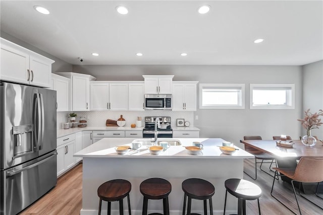 kitchen with stainless steel appliances, light hardwood / wood-style floors, tasteful backsplash, and white cabinetry