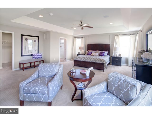 bedroom with a raised ceiling, a walk in closet, ceiling fan, light colored carpet, and a closet