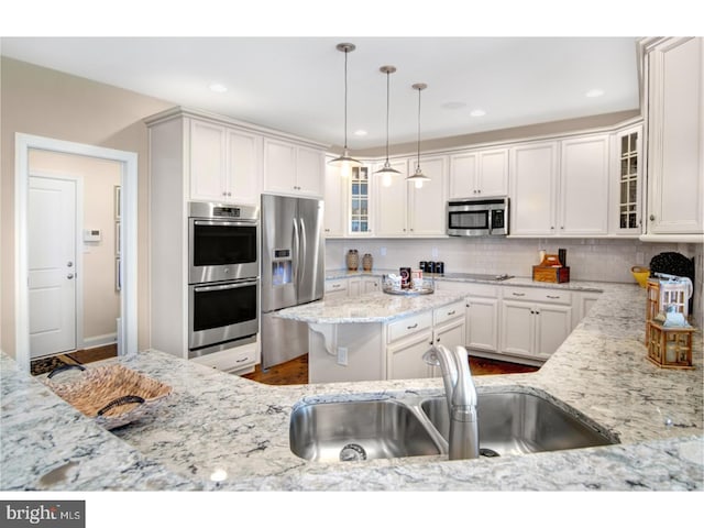 kitchen with appliances with stainless steel finishes, backsplash, sink, white cabinetry, and hanging light fixtures