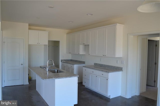 kitchen with white cabinets, light stone countertops, sink, and an island with sink