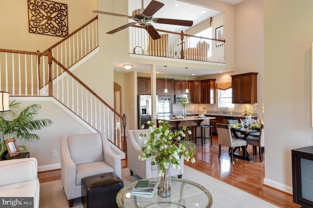 living room featuring a towering ceiling, light hardwood / wood-style flooring, and ceiling fan