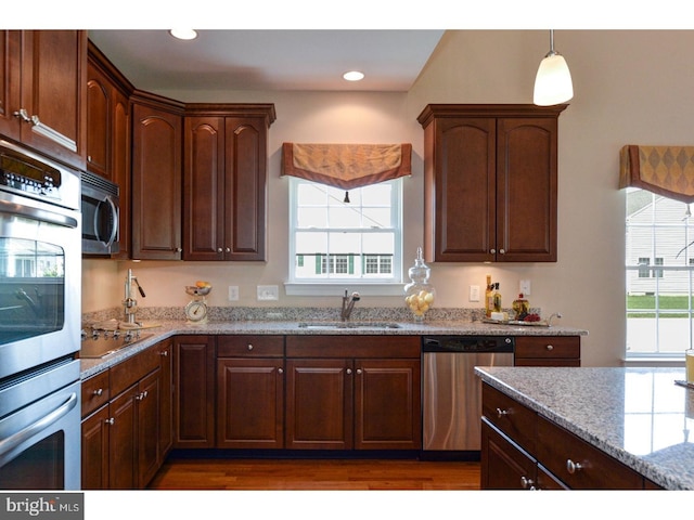 kitchen with dark wood-type flooring, sink, appliances with stainless steel finishes, pendant lighting, and light stone countertops