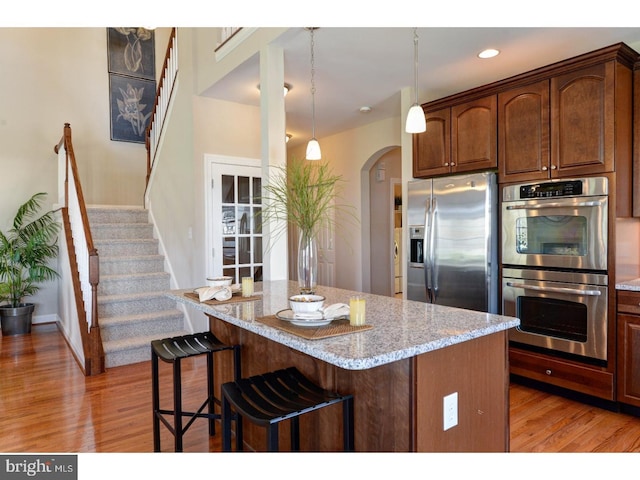 kitchen with stainless steel appliances, a center island, a kitchen breakfast bar, light stone counters, and decorative light fixtures