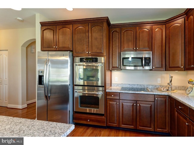 kitchen with dark hardwood / wood-style flooring, light stone counters, and appliances with stainless steel finishes