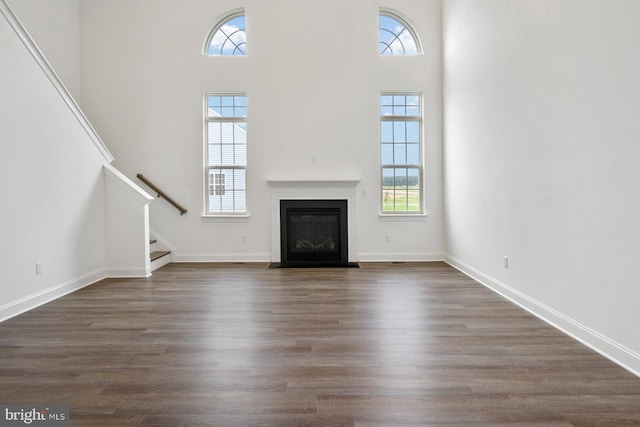 unfurnished living room with a towering ceiling and dark hardwood / wood-style flooring