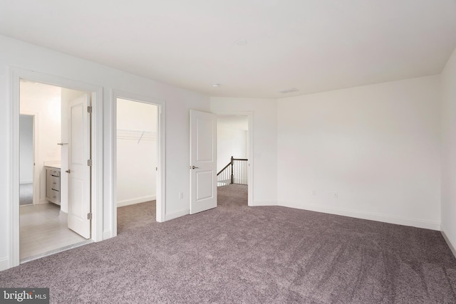 unfurnished bedroom featuring a spacious closet, a closet, ensuite bathroom, and light carpet