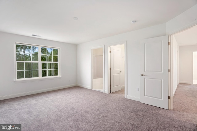 unfurnished bedroom featuring a walk in closet and light colored carpet