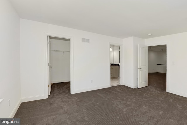 unfurnished bedroom featuring dark carpet, a walk in closet, and a closet