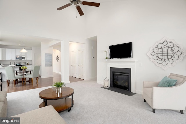 carpeted living room with ceiling fan and a high ceiling