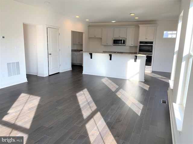 kitchen featuring white cabinetry, dark wood-type flooring, a breakfast bar area, a center island with sink, and appliances with stainless steel finishes