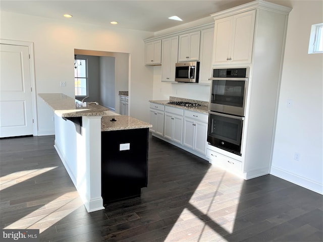 kitchen with appliances with stainless steel finishes, dark hardwood / wood-style flooring, and a center island with sink