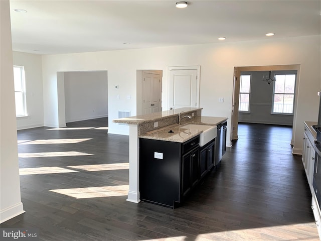 kitchen featuring light stone counters, sink, a center island with sink, dark hardwood / wood-style floors, and white cabinetry