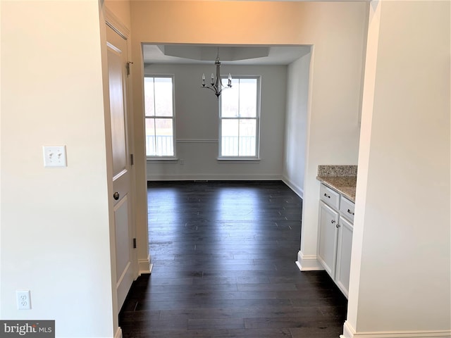 unfurnished dining area with dark wood-type flooring and an inviting chandelier