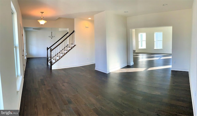 empty room with dark hardwood / wood-style flooring and a notable chandelier