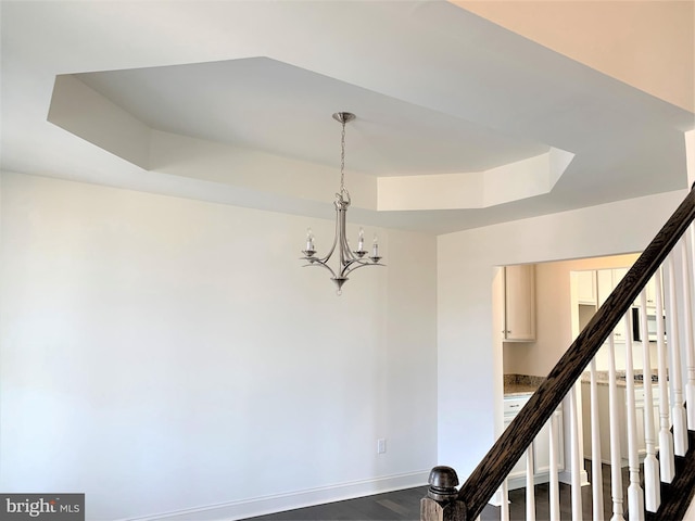 staircase featuring a raised ceiling, wood-type flooring, and an inviting chandelier