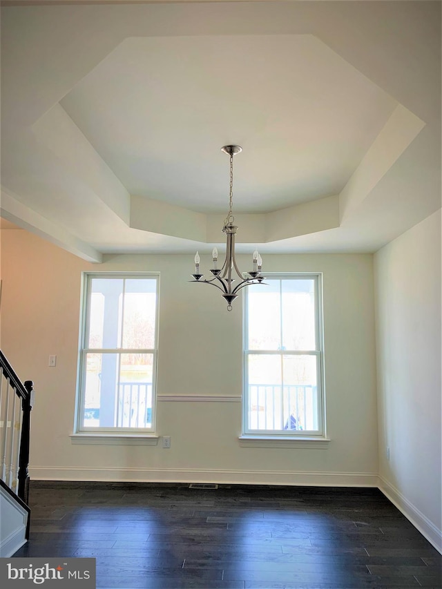 unfurnished dining area with a raised ceiling, plenty of natural light, dark hardwood / wood-style flooring, and a notable chandelier