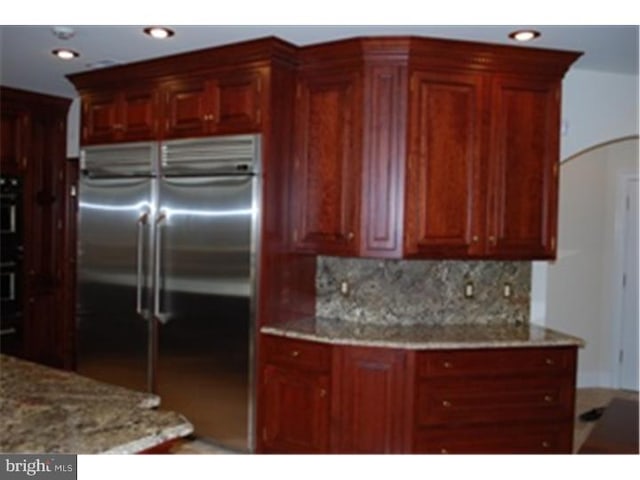 kitchen with stainless steel built in refrigerator, backsplash, double oven, and light stone countertops