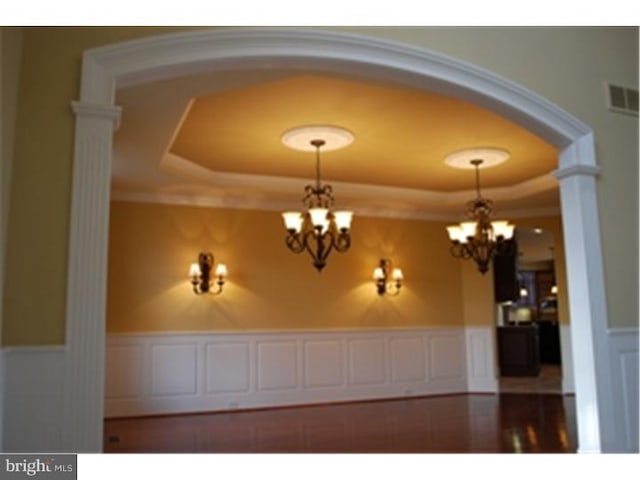 interior space featuring a chandelier, decorative columns, and a raised ceiling