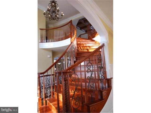 staircase with crown molding and a chandelier