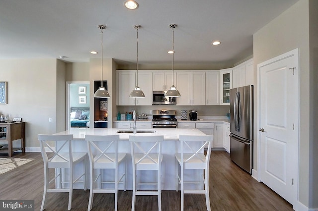 kitchen with stainless steel appliances, a kitchen island with sink, dark wood-type flooring, pendant lighting, and white cabinets