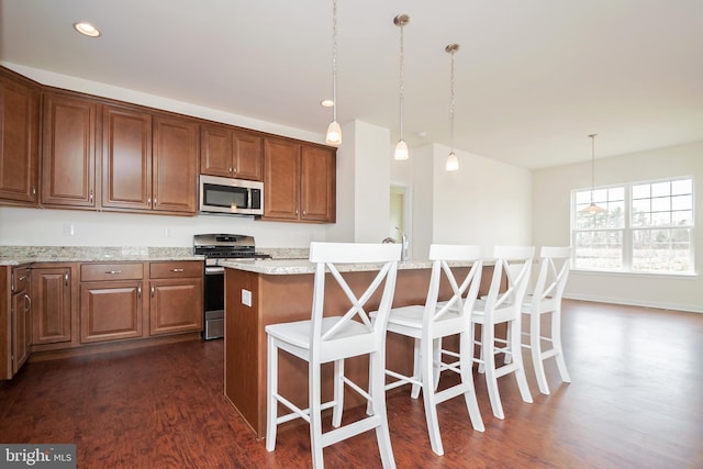 kitchen featuring light stone countertops, stainless steel appliances, dark wood-type flooring, pendant lighting, and a kitchen island