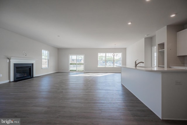 unfurnished living room featuring sink, a chandelier, and dark hardwood / wood-style floors