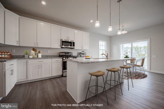 kitchen with dark wood-type flooring, decorative light fixtures, a center island with sink, white cabinets, and appliances with stainless steel finishes