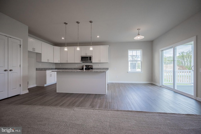 kitchen featuring an island with sink, pendant lighting, wood-type flooring, white cabinets, and appliances with stainless steel finishes