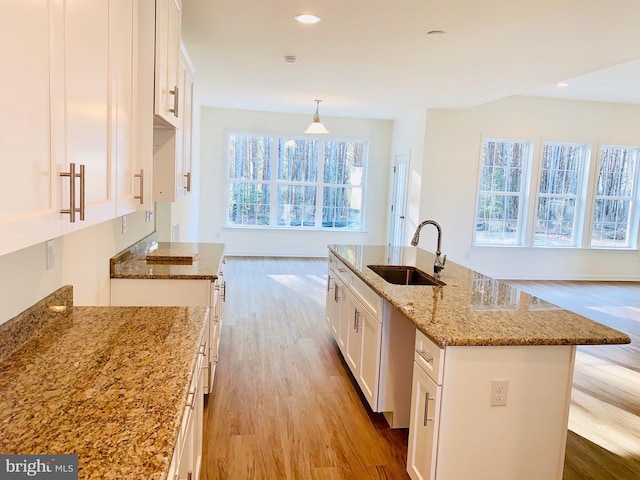 kitchen with white cabinets, sink, an island with sink, and light wood-type flooring