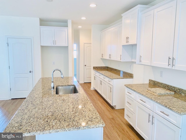 kitchen with light stone counters, sink, a center island with sink, light hardwood / wood-style floors, and white cabinetry