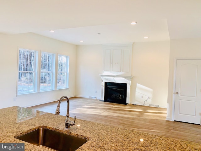 kitchen with white cabinetry, light stone counters, sink, and light hardwood / wood-style flooring