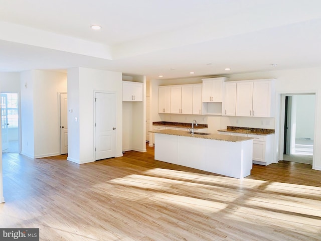 kitchen featuring light wood-type flooring, white cabinetry, a kitchen island with sink, and sink