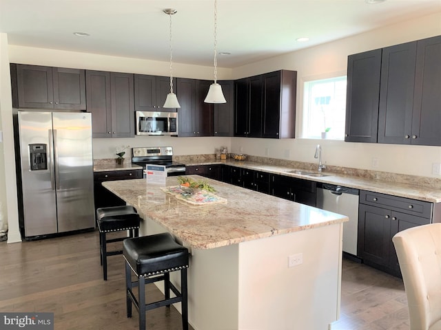 kitchen with appliances with stainless steel finishes, sink, wood-type flooring, pendant lighting, and a kitchen island