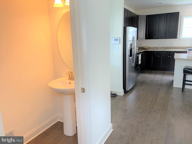 interior space with a kitchen bar, stainless steel fridge with ice dispenser, dark hardwood / wood-style flooring, and light stone countertops