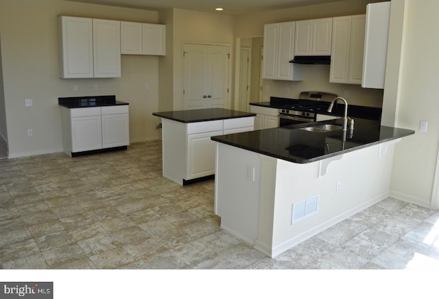 kitchen with a kitchen bar, stainless steel range, sink, a center island, and white cabinetry